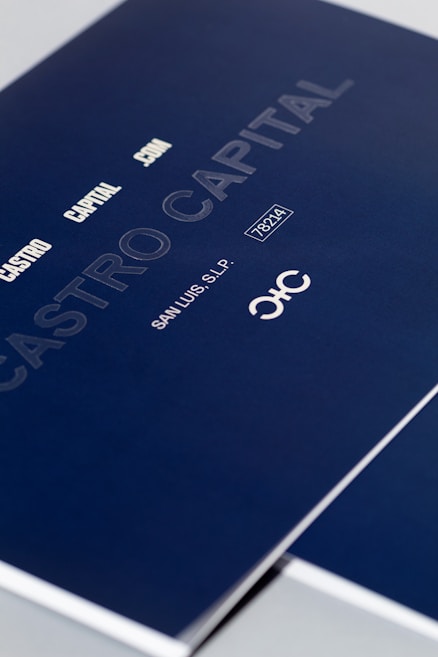 A close-up of a sleek dark blue cover design featuring text in white and light gray, including 'CASTRO CAPITAL .COM', 'SAN LUIS, S.L.P.', and a number '78214'. The design includes a stylized logo with interlocking letters.