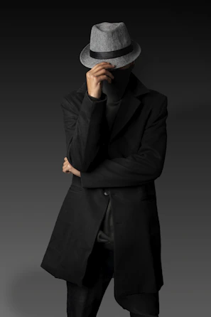A man in a black coat and hat with his hands on his face