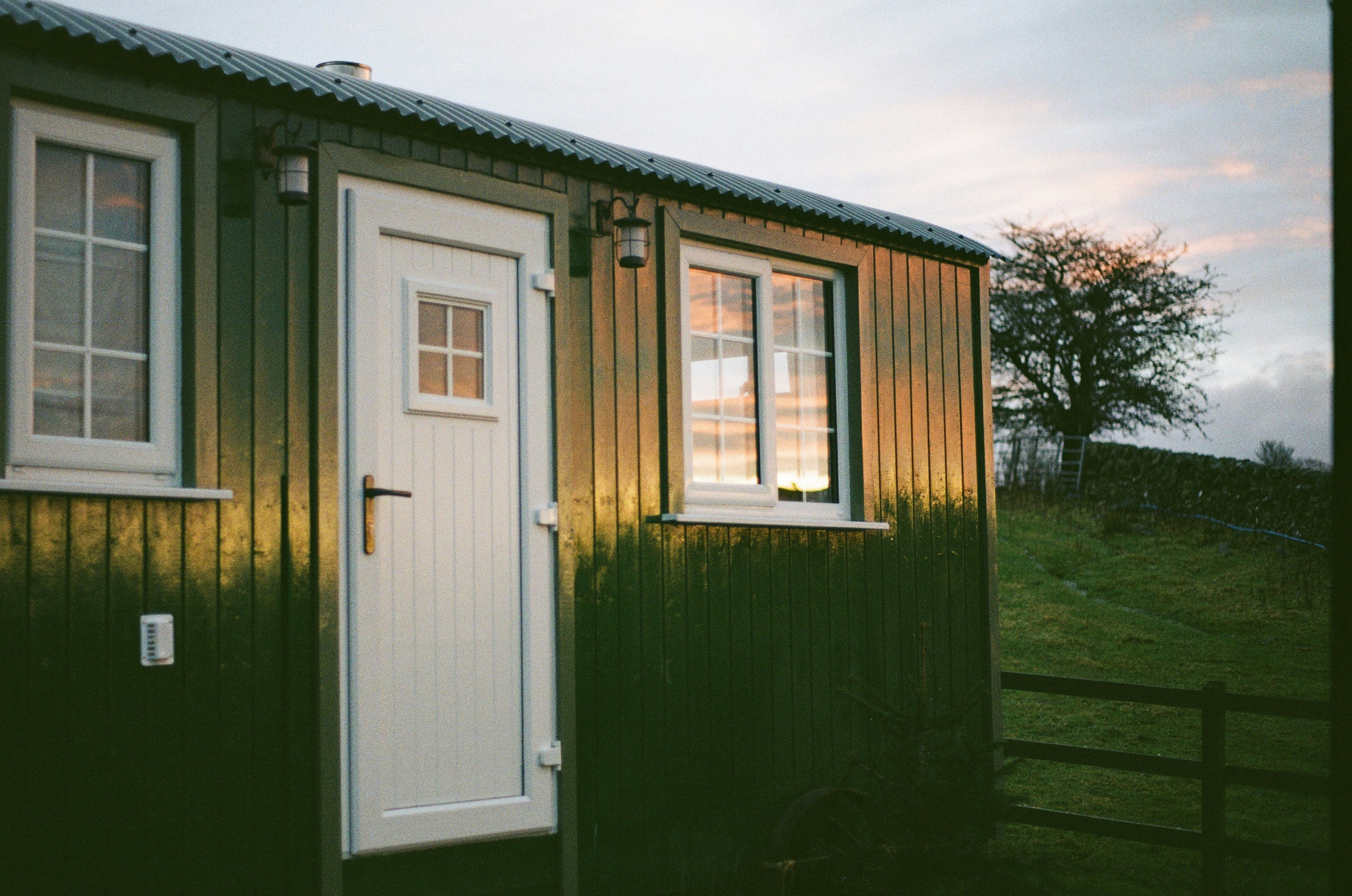 a large brick building with a green door, Morning light on a shepherds hut in Scotland.