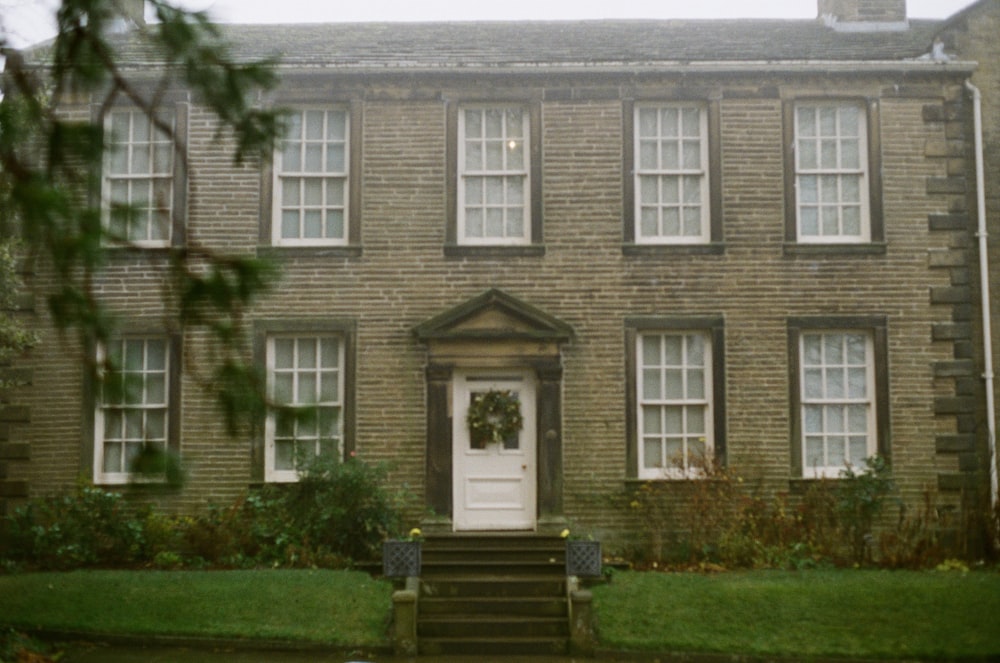 a large brick building with grass in front of a house with Brontë Parsonage Museum in the background