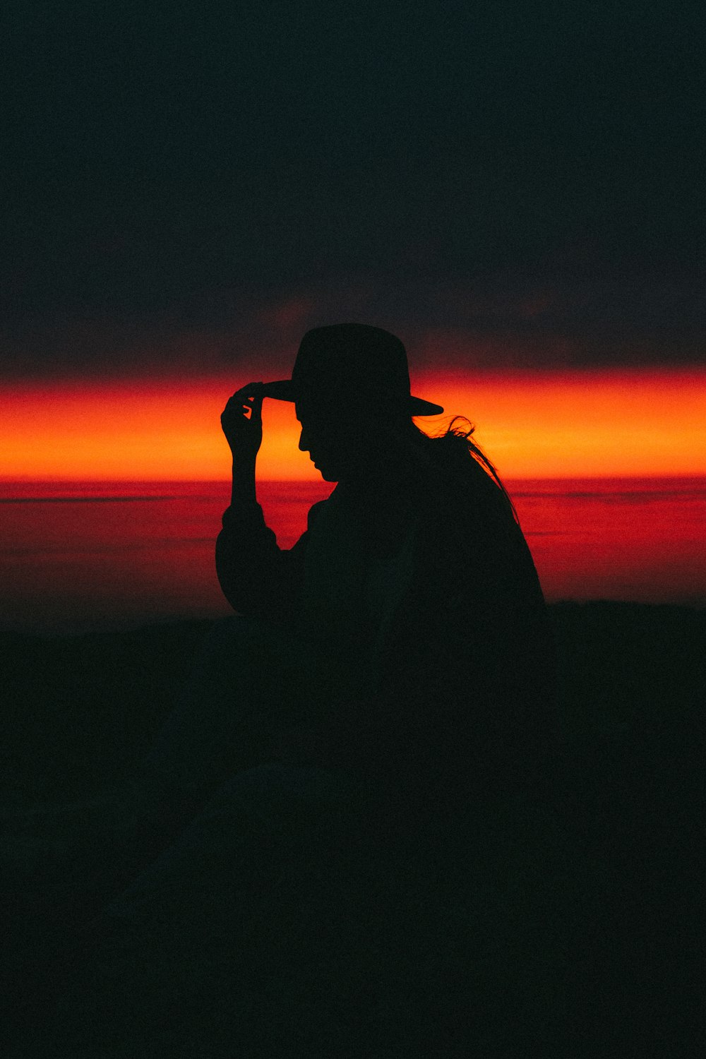 Una persona seduta su una collina con un tramonto sullo sfondo