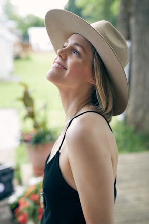 a woman wearing a hat standing in front of a tree