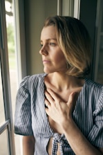 a woman looking out a window with her hand on her chest