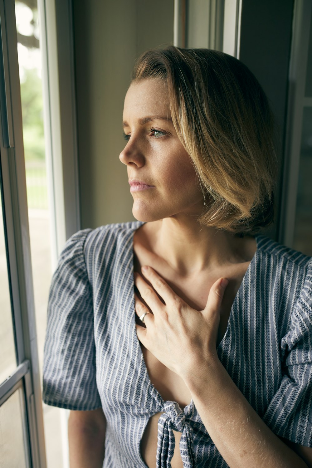 a woman looking out a window with her hand on her chest