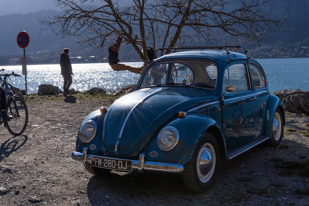 a blue vw bug parked next to a lake