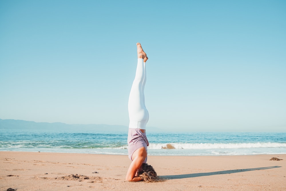 a woman doing a handstand on the beach