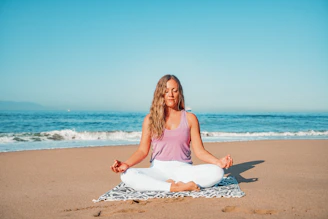 a woman sitting in a yoga position on the beach