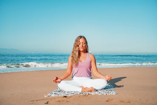 a woman sitting in a yoga position on the beach