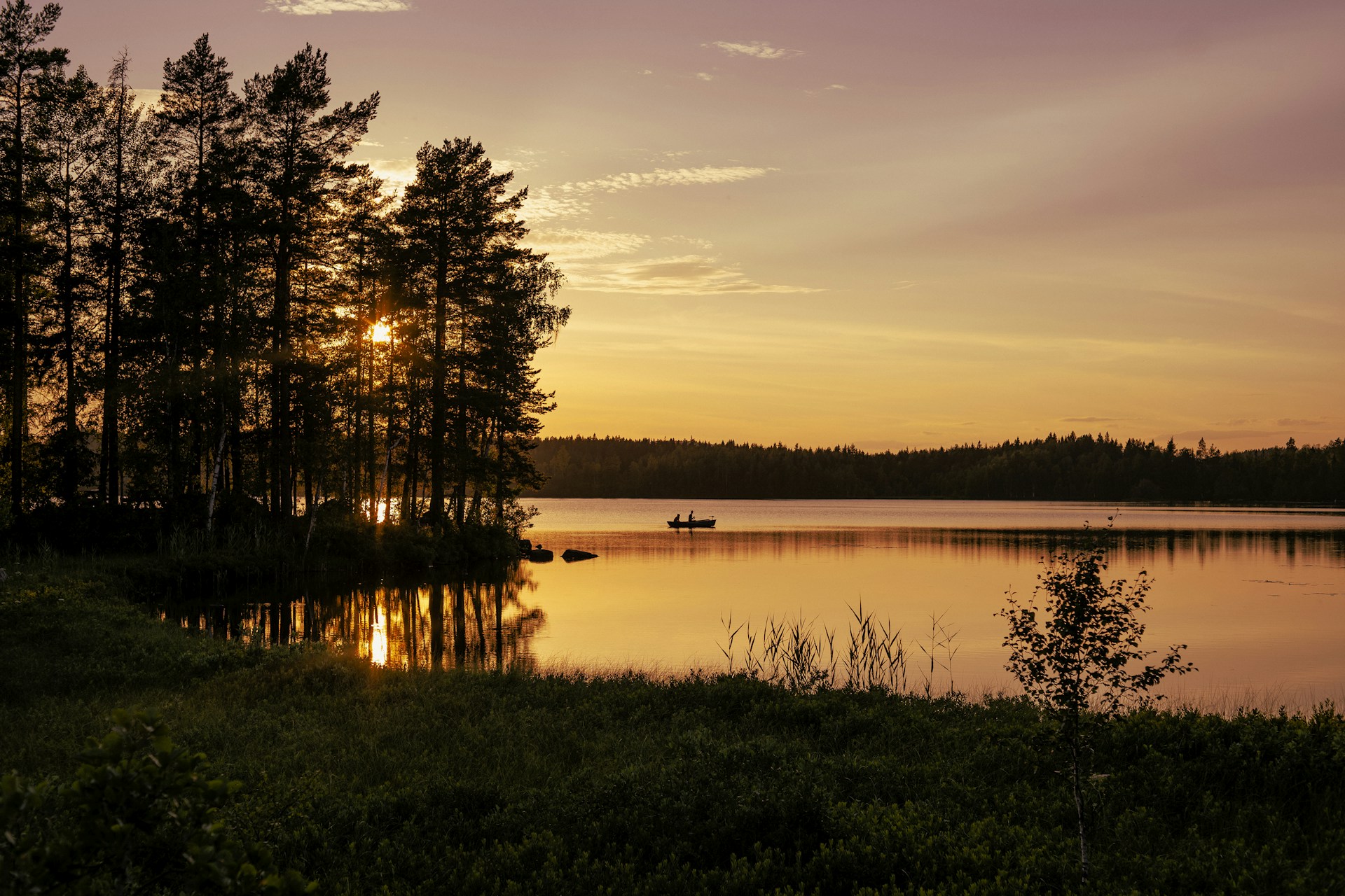 the sun is setting over a lake with a boat in it