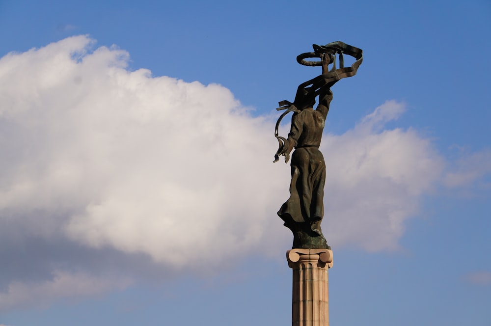 a statue of a woman holding a hat on top of a pillar