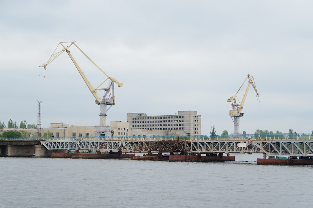 two cranes are on a bridge over a body of water