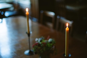 Two candles flickering softly on a wooden table set for an intimate evening ritual.