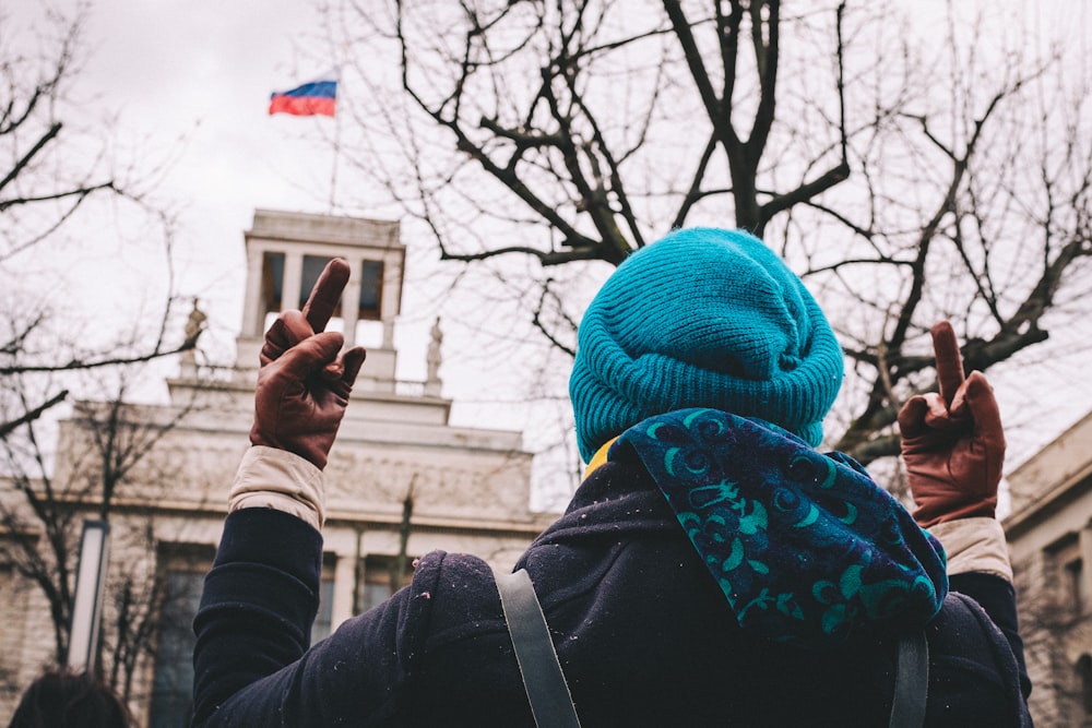 a person wearing a blue hat and scarf making the peace sign