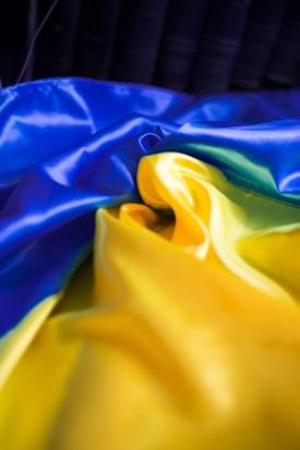A vibrant, flowing fabric in vivid blue and yellow hues. The fabric appears smooth and shiny, creating a dynamic contrast between the colors. The texture of the material is soft, and the way it is arranged suggests movement and fluidity.