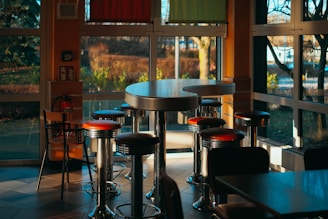 a restaurant with tables and stools in front of a large window