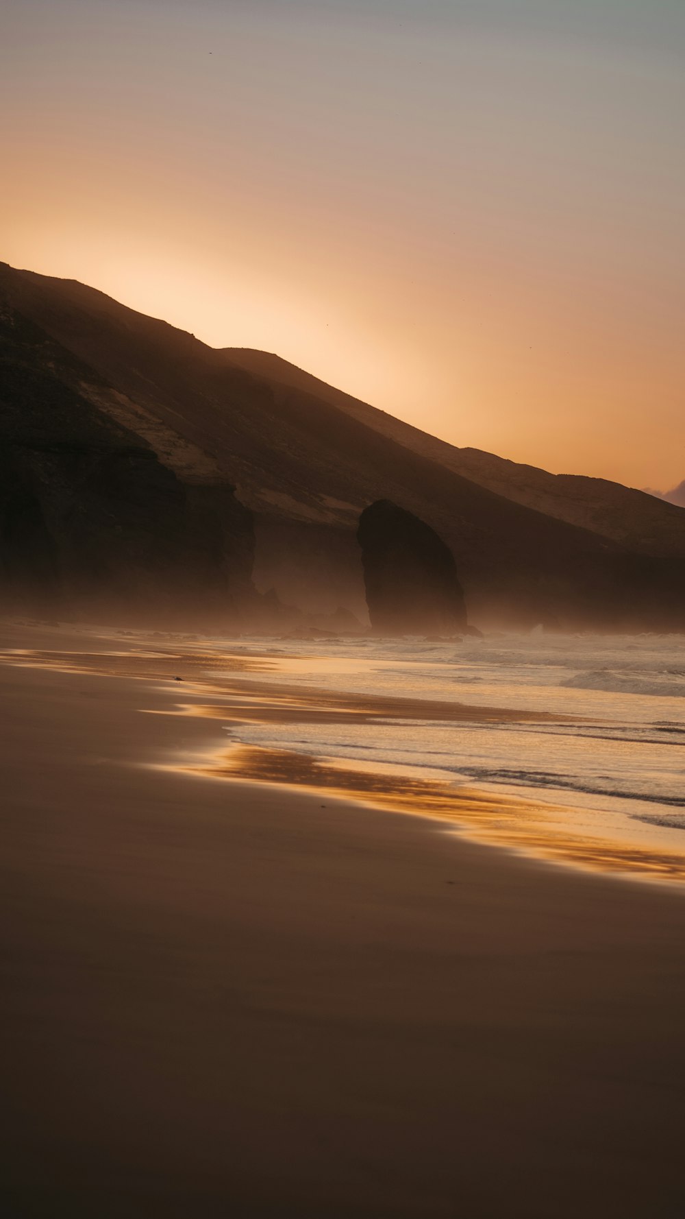 the sun is setting on the beach with a mountain in the background