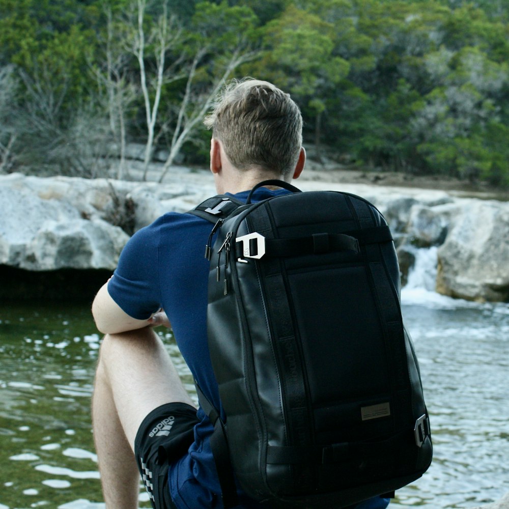 a man with a backpack sitting by a river