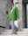 A fashionably dressed person stands on marble stairs. They are wearing a vibrant green blazer, light blue flared jeans, and a white headscarf. The setting appears modern, with large stones and reflective surfaces in the background.