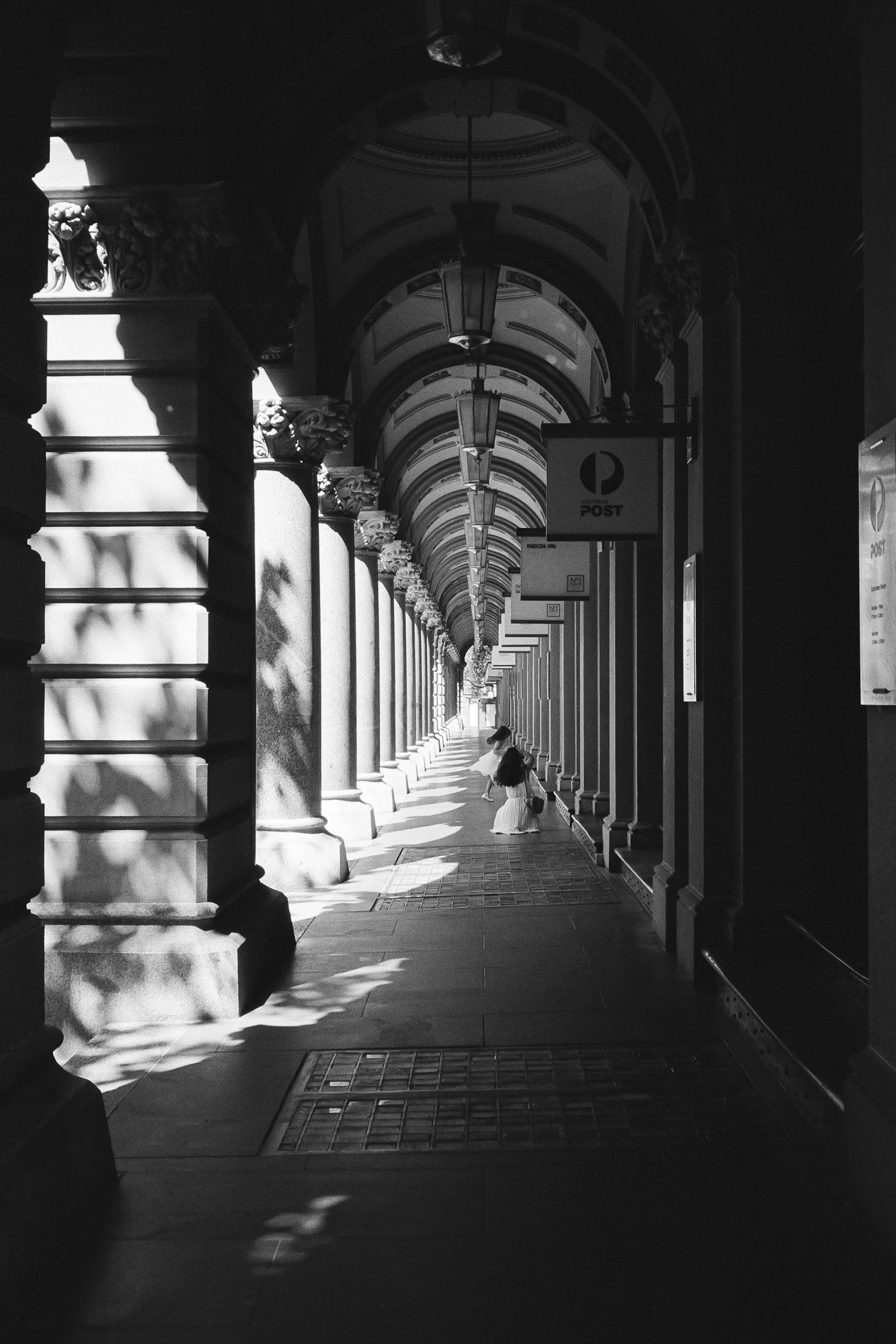 Person waiting alone on a bench in a Sydney building corridor, black and white