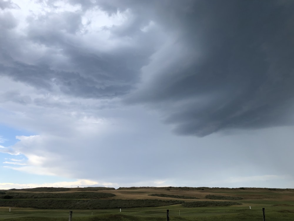 a large storm cloud looms over a green field