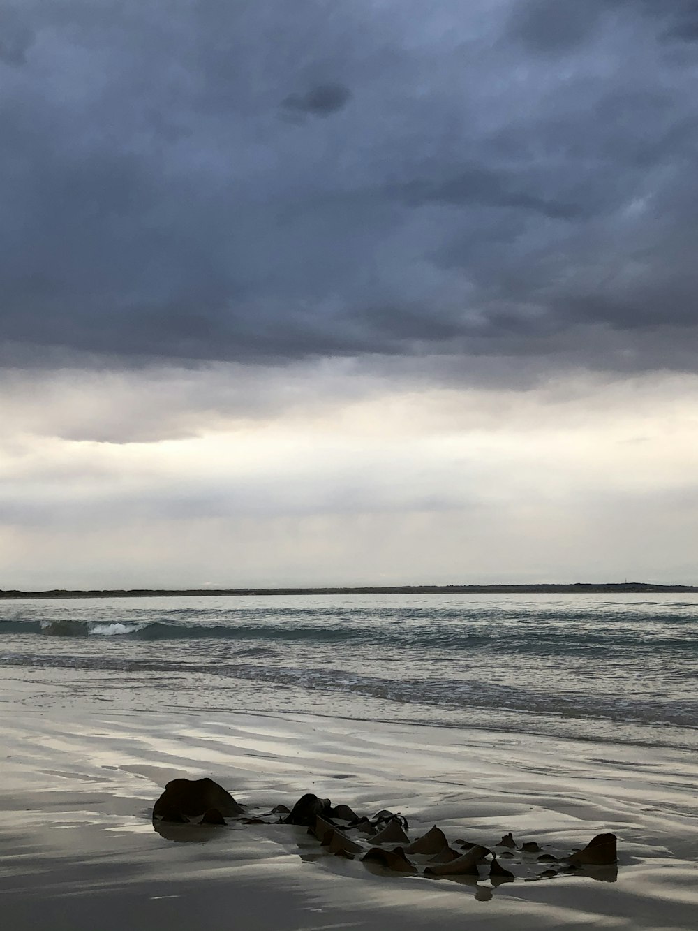 a cloudy day at the beach with rocks in the foreground