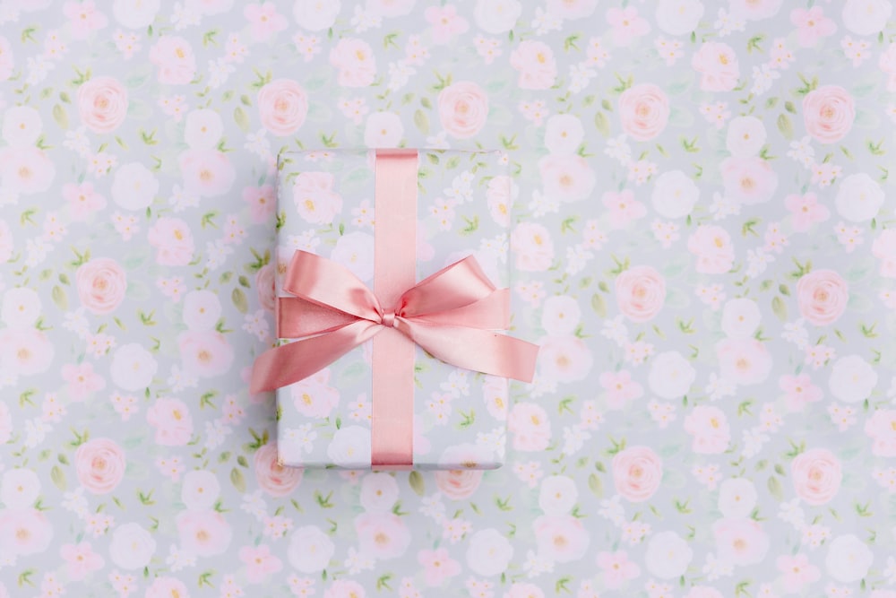 a present wrapped in pink ribbon on a floral background