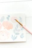 Soft pastel pink rounded card featuring a stylized illustration of a camera and paintbrushes