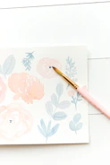 Soft pastel pink rounded card featuring a stylized illustration of a camera and paintbrushes