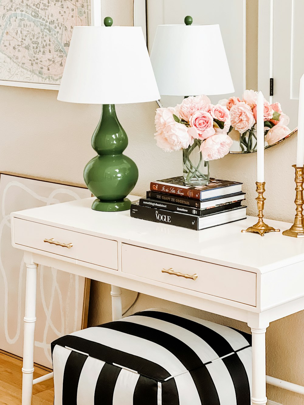 a white desk topped with a lamp and a green vase filled with flowers