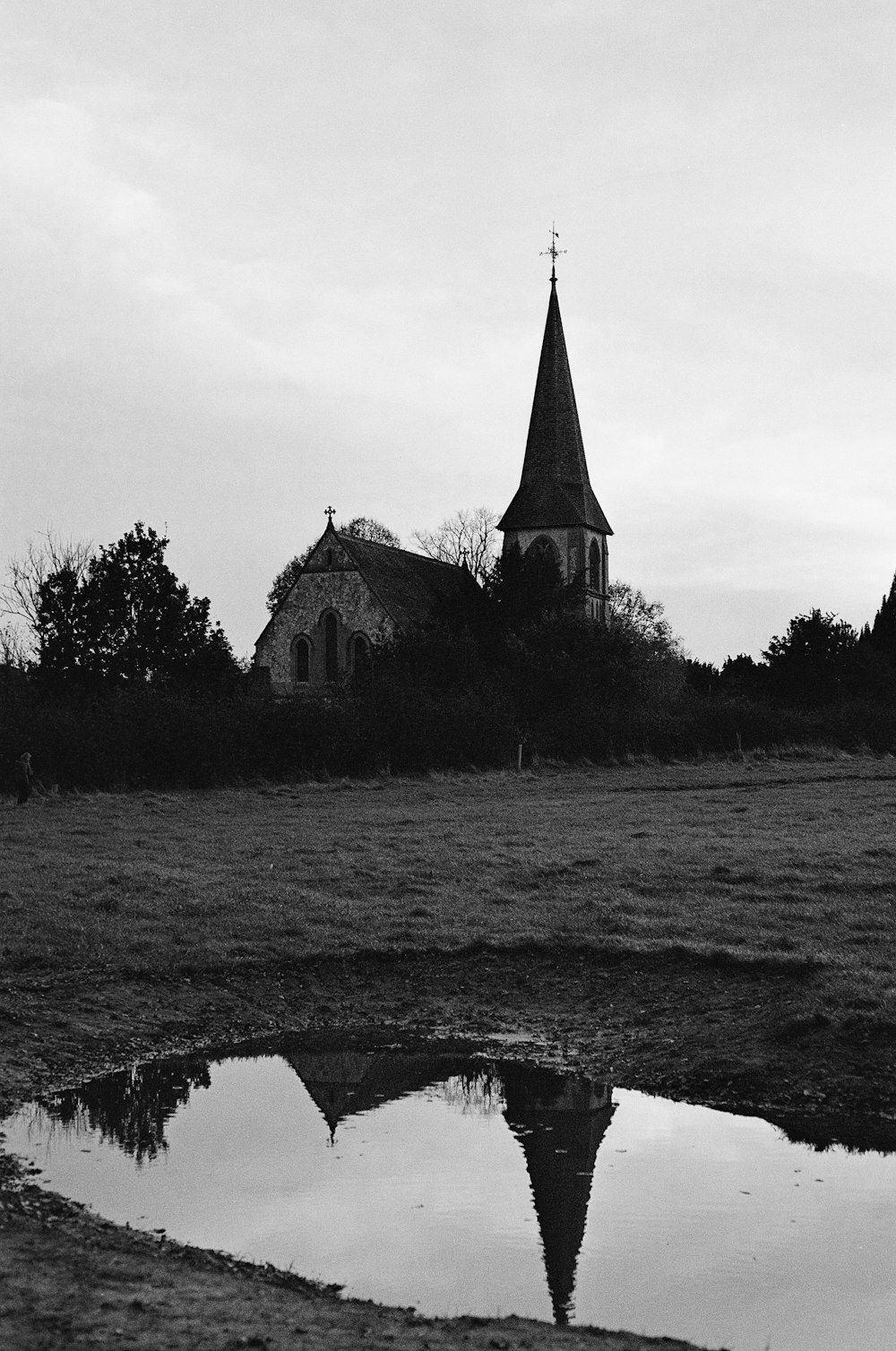 a black and white photo of a church and its reflection in a puddle
