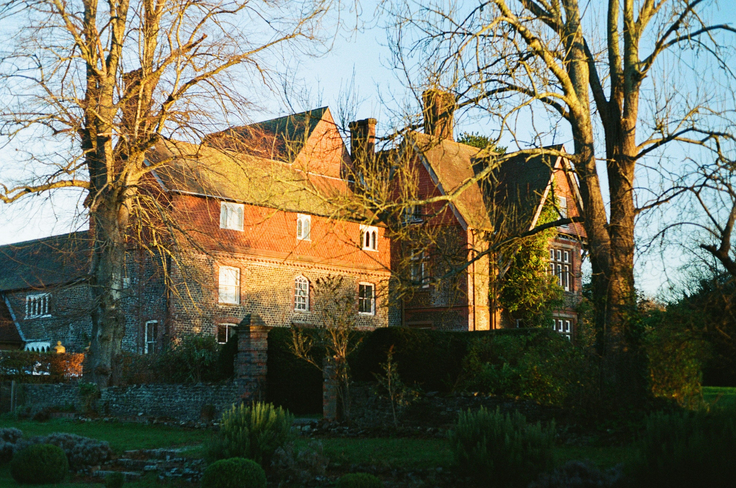 a large brick house surrounded by trees and bushes, Barren trees around the manor.
