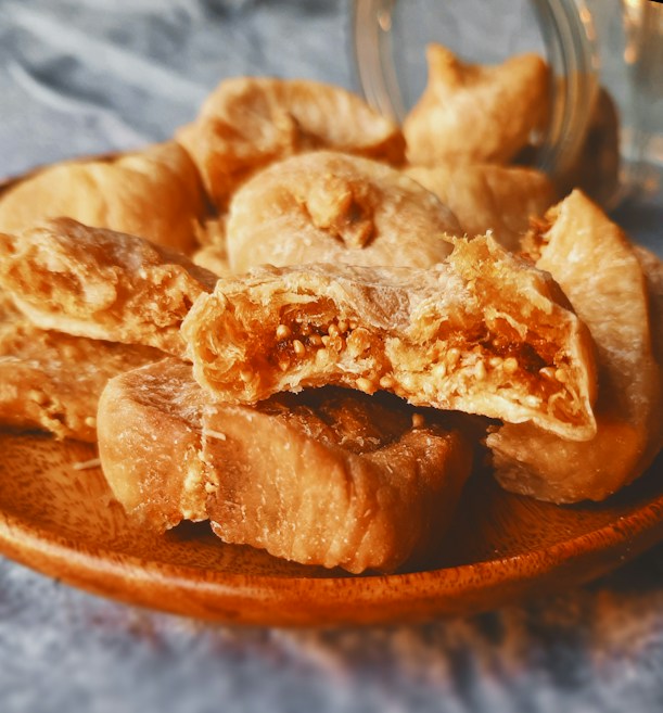 A close-up view of dried figs on a wooden plate, showing their textured surface and seeds. The image conveys a rustic and natural feel, capturing the figs' rich, golden-brown tones.