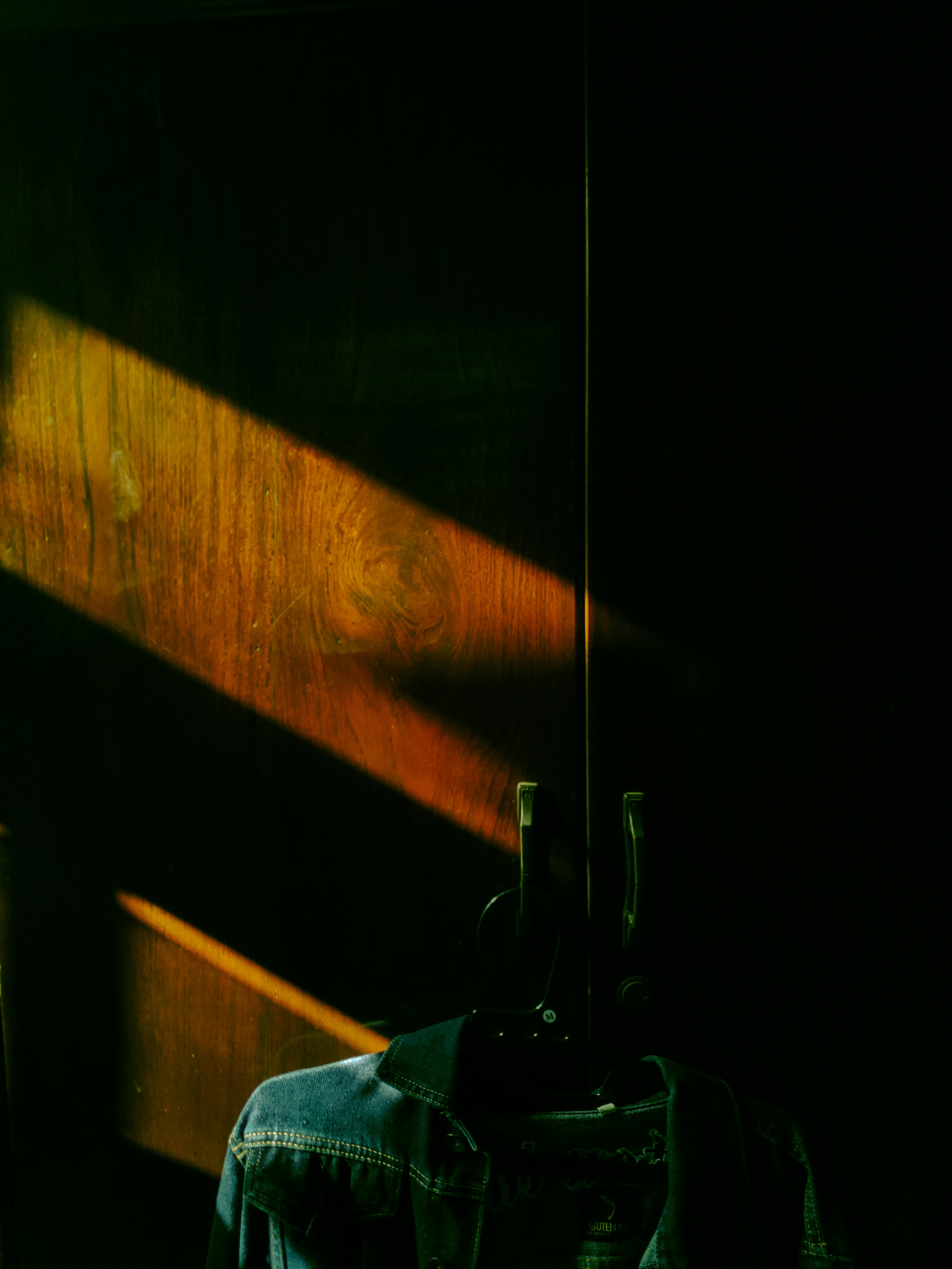 Denim jacket on dark hanger with moody studio lighting and deep shadows