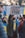 A person wearing a black mask holds a sign that reads 'I STAND WITH UKRAINE' among a group of people, some of whom are holding or wearing items in blue and yellow, the colors of the Ukrainian flag.