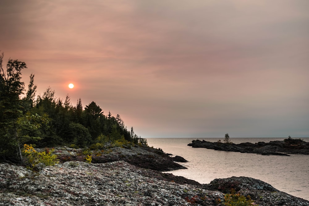 the sun is setting over a rocky shore