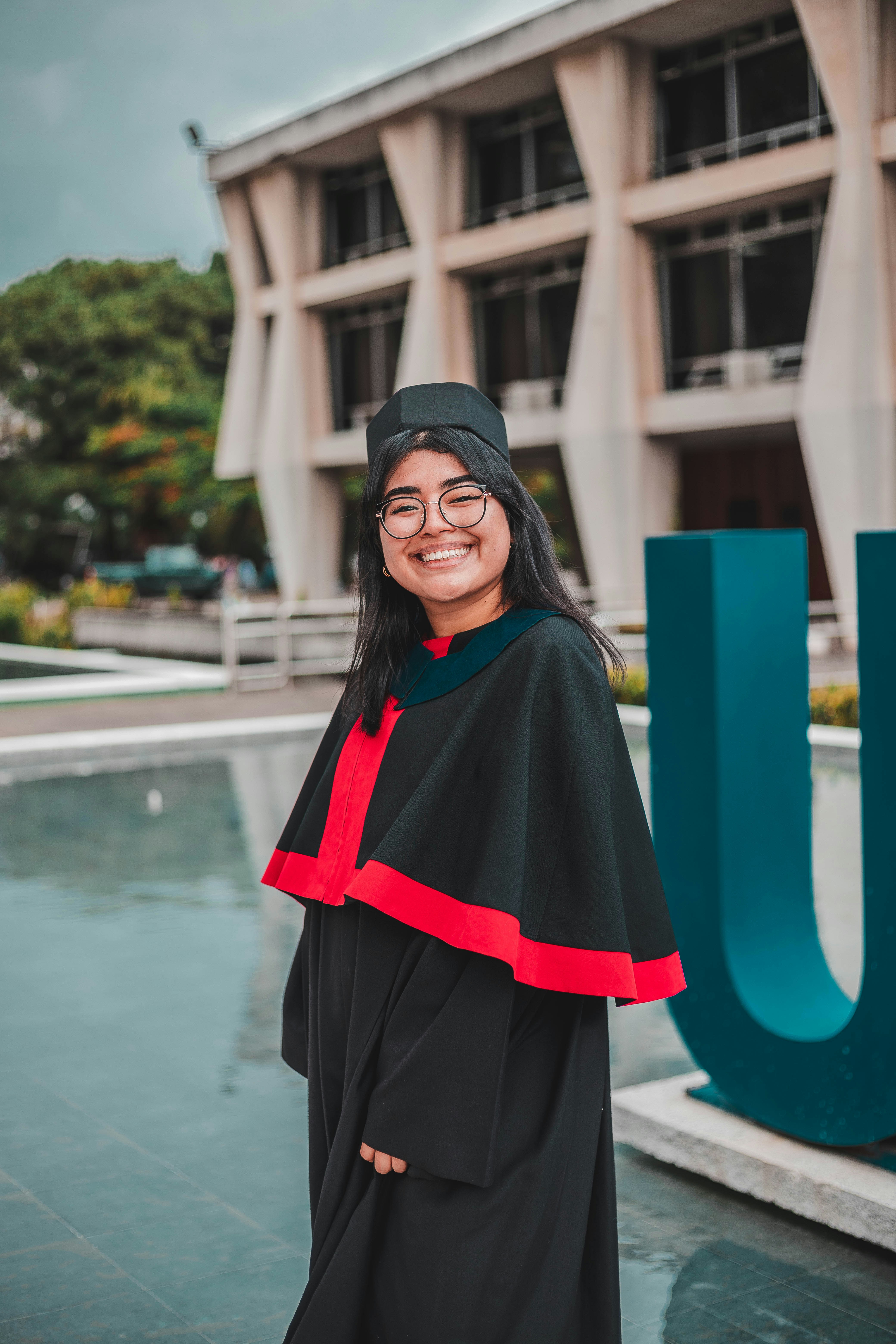 A woman in a graduation gown standing in front of a building photo ...