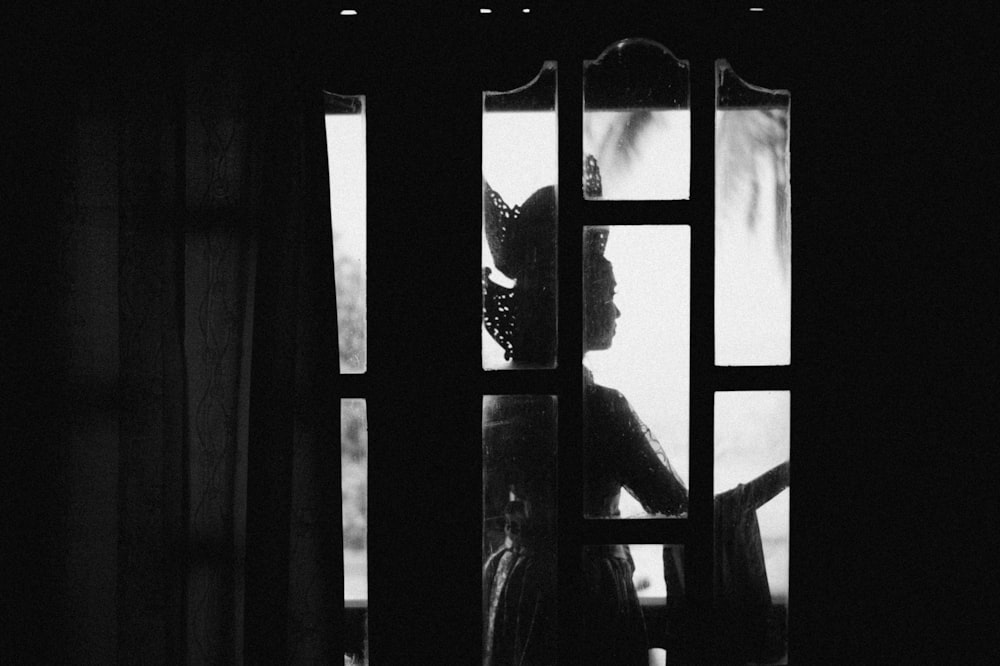 a black and white photo of a woman looking out a window