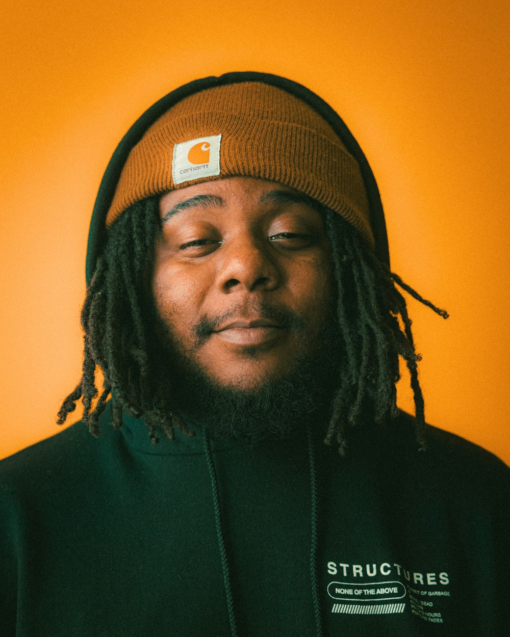 a man with dreadlocks wearing a black shirt and a brown hat