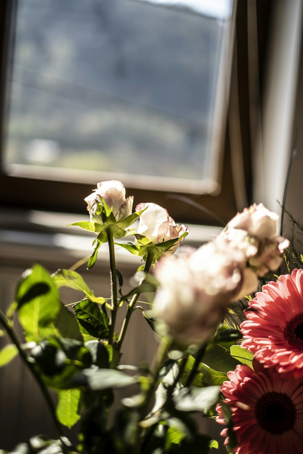 a vase filled with pink and white flowers next to a window