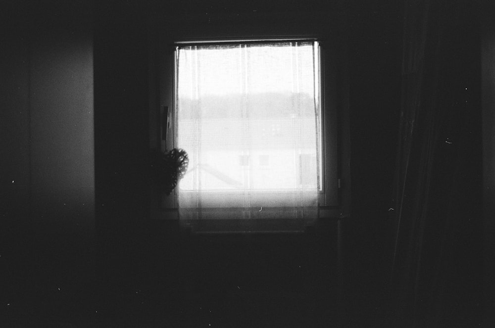 a black and white photo of a person standing in front of a window