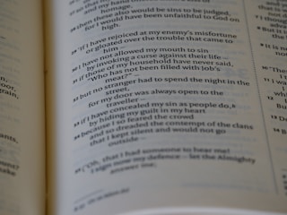 A close-up view of an open book showing text in English. The text is printed in two columns with numbered lines and some words in bold or italic style. The visible portion appears to be from a narrative section or verse format.