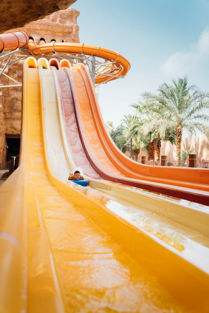 Modern water park slides amid palm trees and sandstone — Qiddiya-style destination