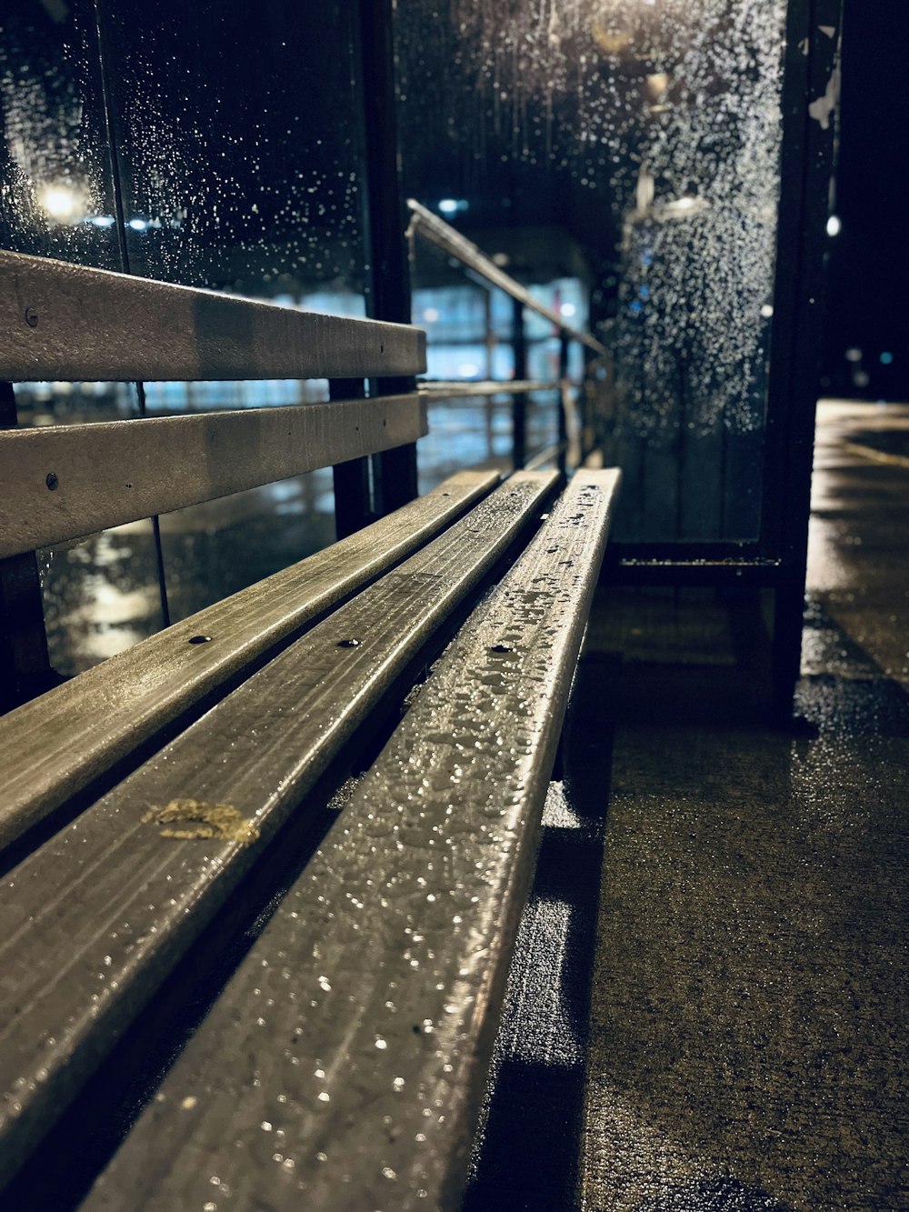a wooden bench sitting next to a window covered in rain