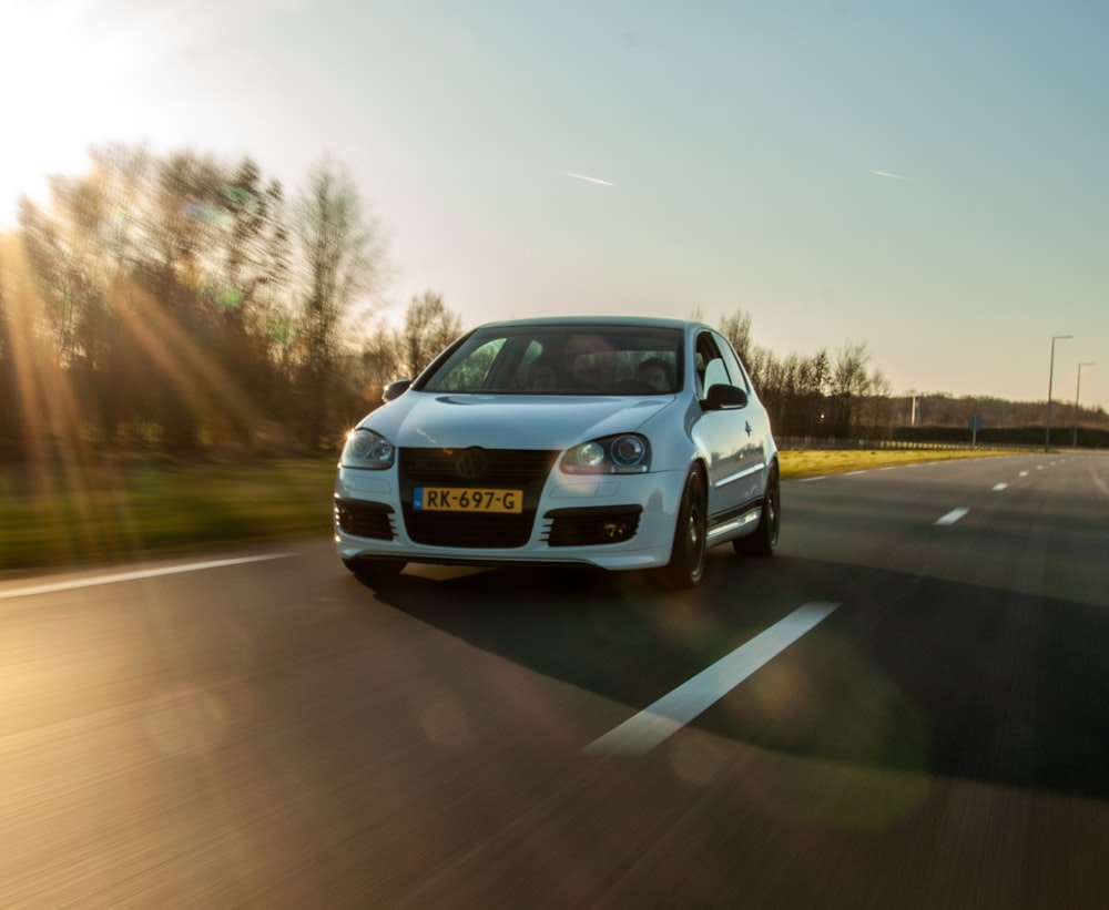 a white car driving down a road next to a forest