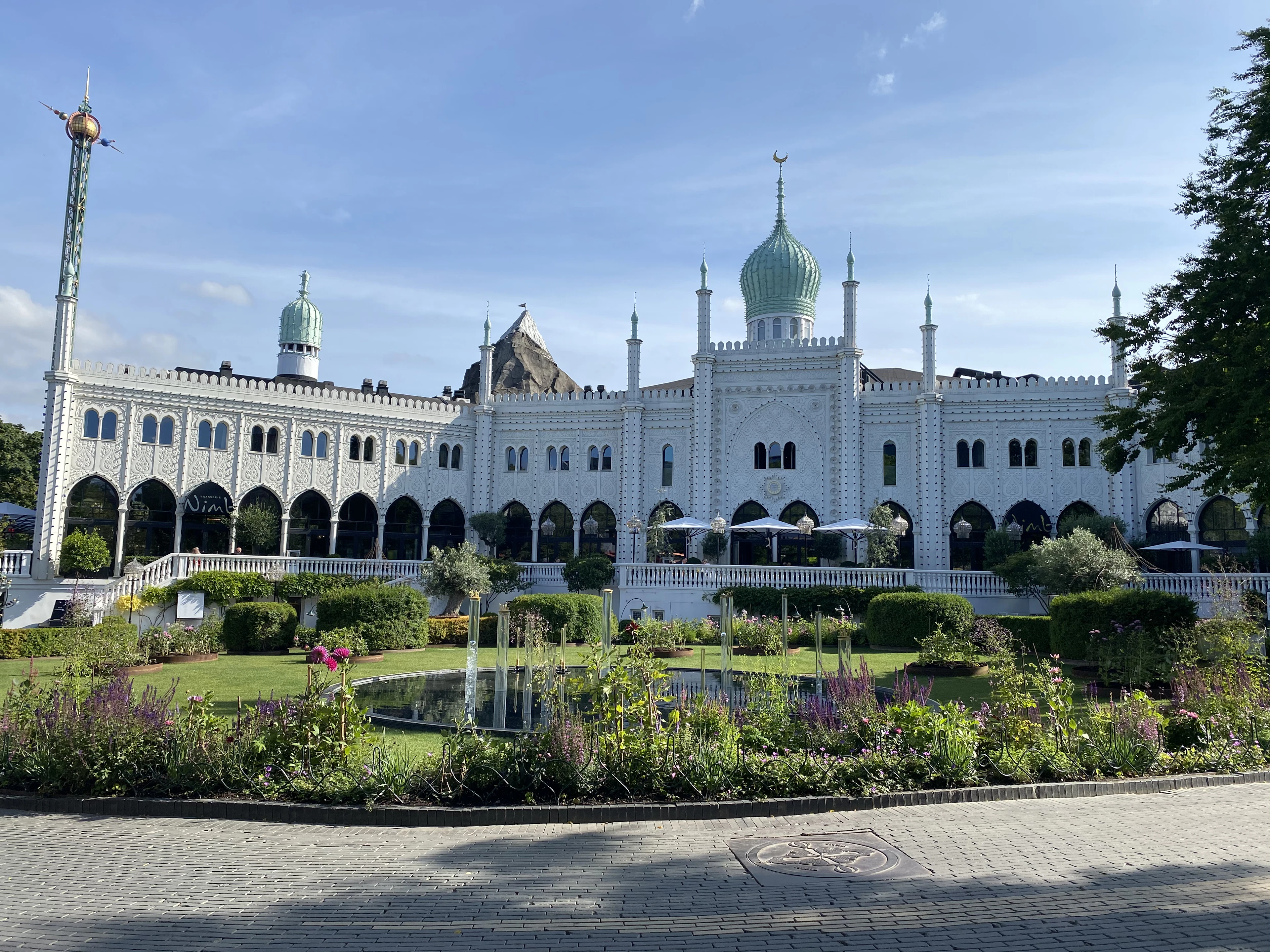 The white Moorish-style palace of the Nimb hotel inside Tivoli Gardens in Copenhagen, its green onion dome and minarets rising above arcaded terraces and a flowerbed-lined pond