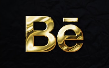Gold metallic text displaying 'Bē' against a black textured background.