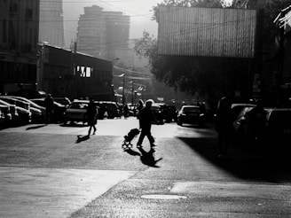 Black and white photo of a city street at dusk, with dramatic shadows and light play.