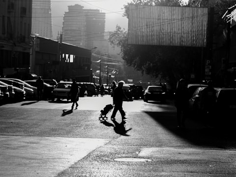 Black and white photo of a city street at dusk, with dramatic shadows and light play.