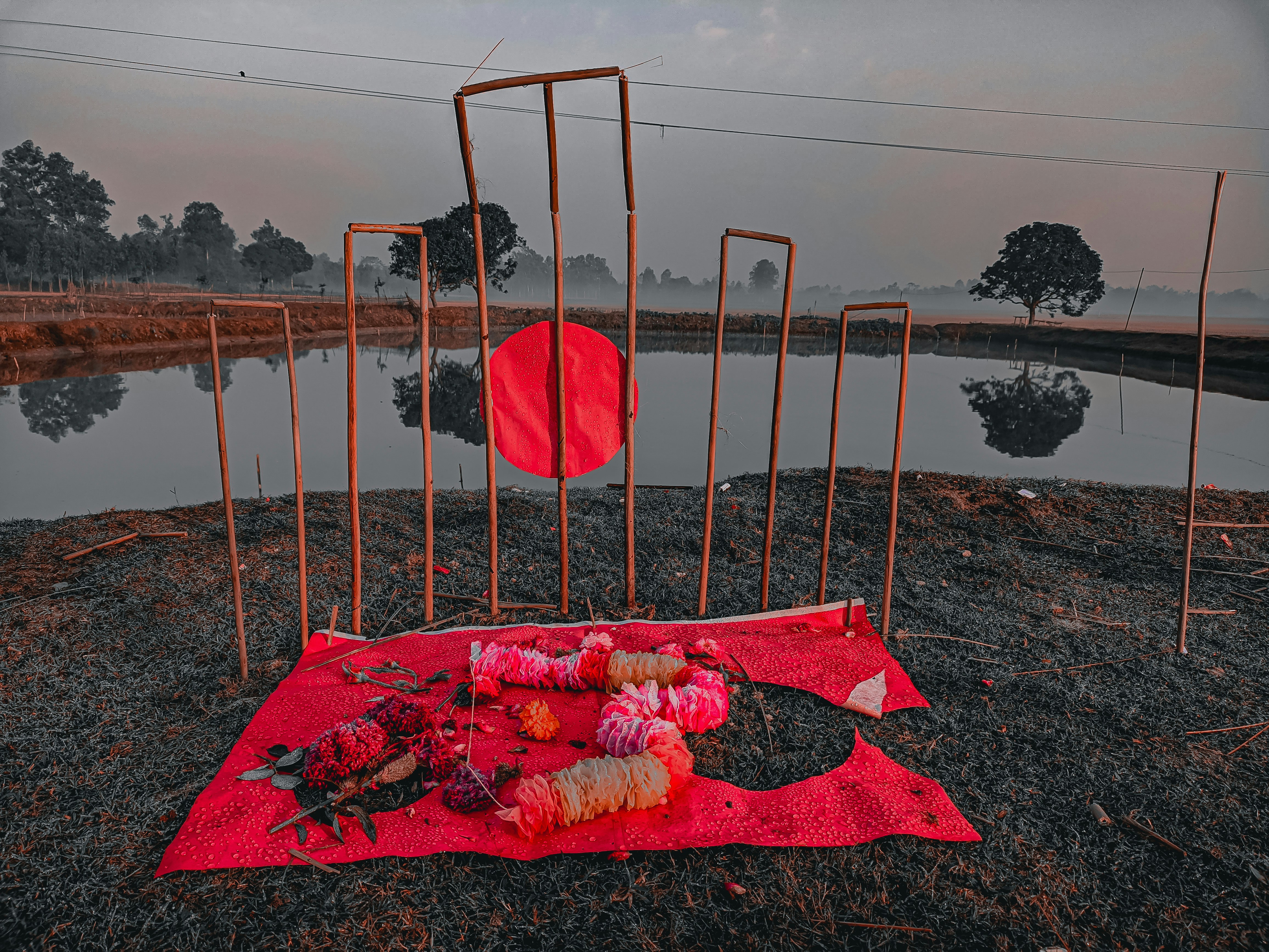 A red blanket on the ground next to a body of water photo Free
