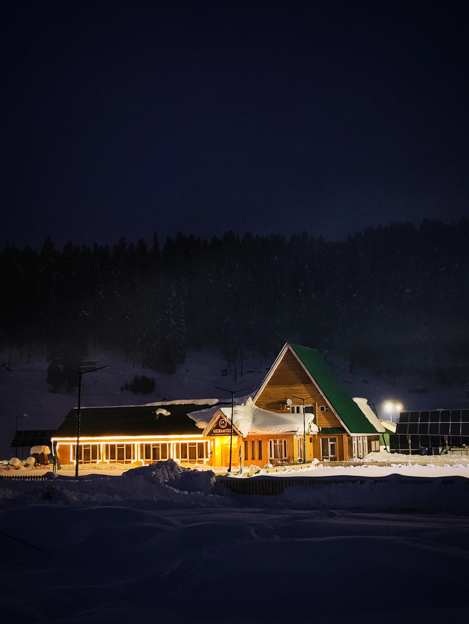 A lit timber building standing alone in deep snow at night